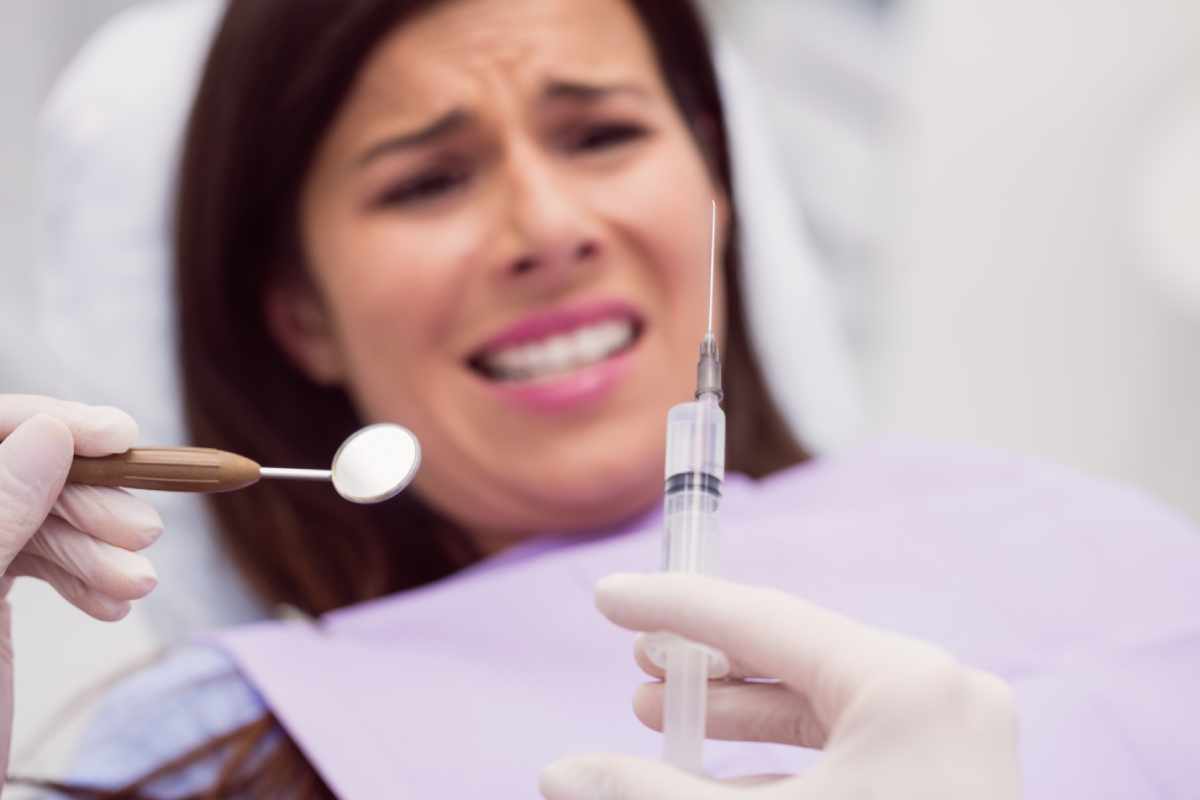 A women looks nervously at a dentist needle as she is about to get an injection